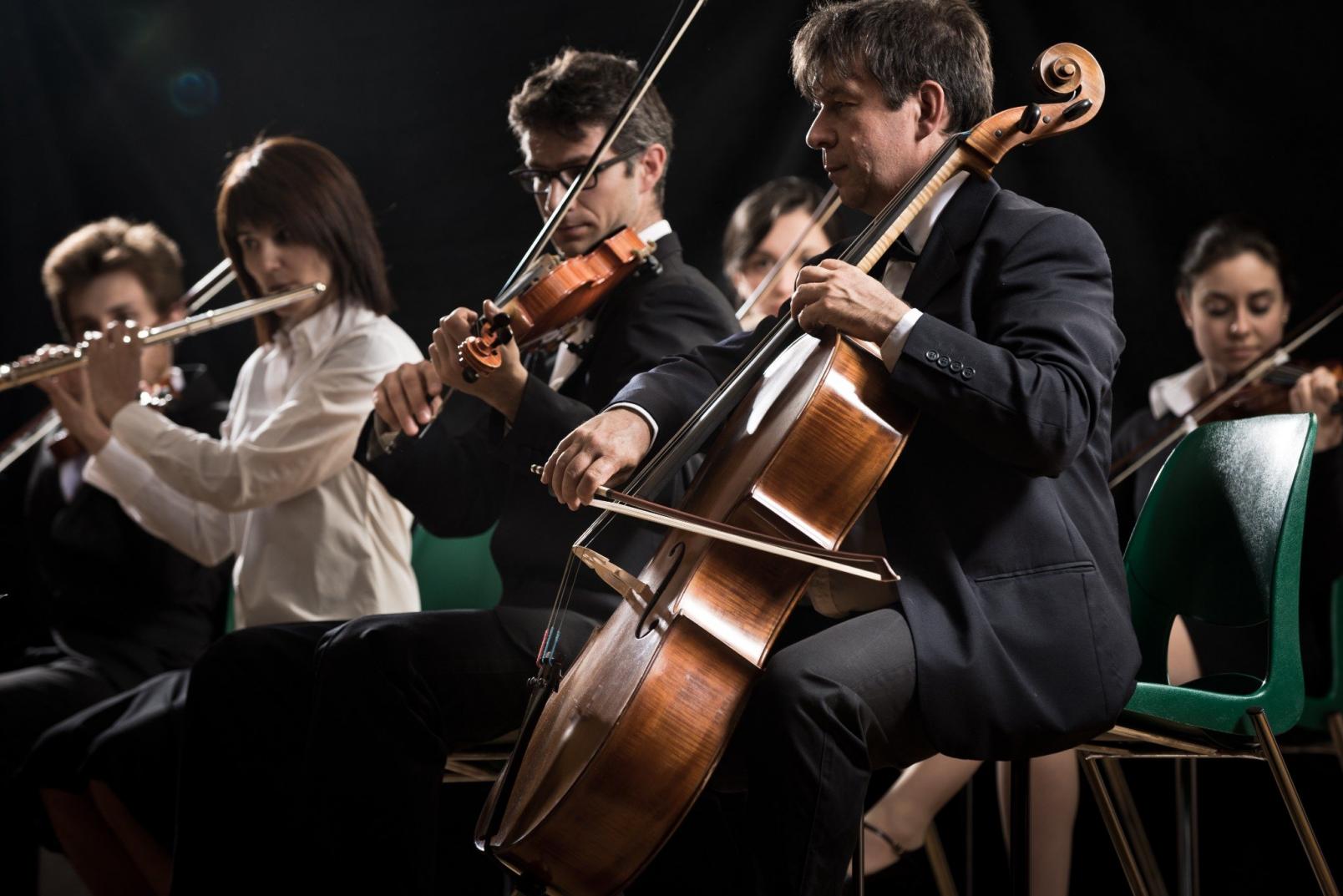 Ausschnitt eines Orchesters. Darauf zu sehen drei Personen, die live spielen. 