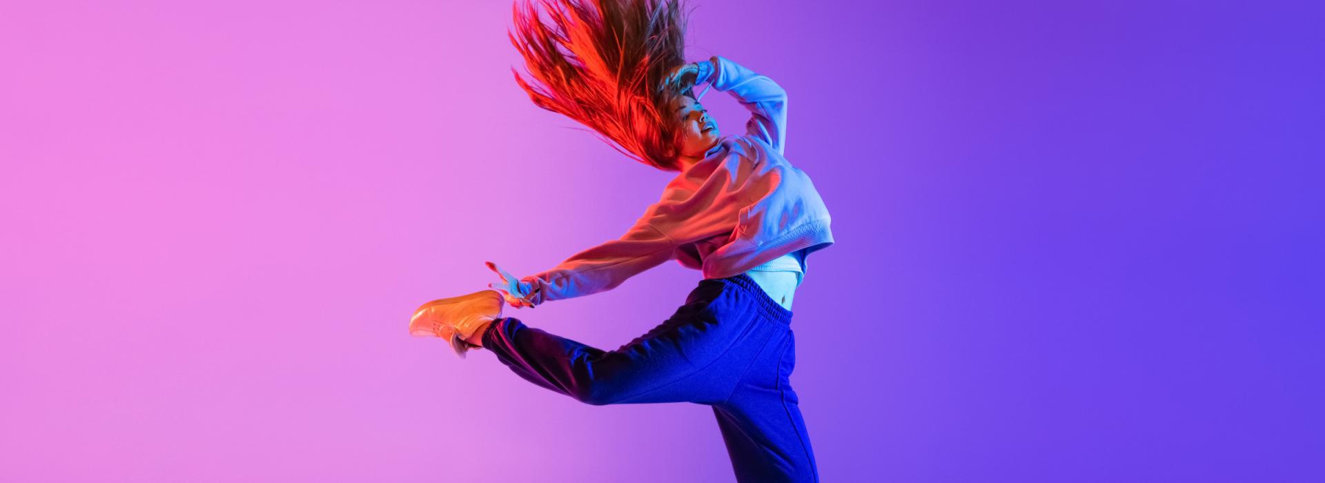 Zeigt eine tanzende, junge Frau vor einem Pink-Blauen Hintergrund