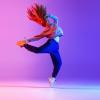 Zeigt eine tanzende, junge Frau vor einem Pink-Blauen Hintergrund